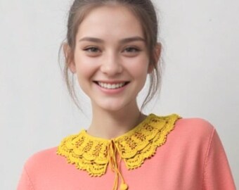 Puede incluir: Un suéter de color coral con mangas cortas y un cuello amarillo brillante con ribete de encaje. El cuello está atado con una cuerda amarilla y dos bolitas amarillas. La mujer sonríe.