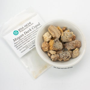 May include: A small white bowl filled with Mayan Dark Copal resin pieces. The resin is a natural incense and is considered the most desirable for its rich aroma. The label reads "Soul Niche Simply good for the soul. Mayan Dark Copal Natural Resin. For use as incense. Burn over charcoal tabs. Dark copal is considered the most desirable for its rich aroma. Contents: Copal. Origin Indonesia. Burn responsibly. Do not leave unattended. Keep out of reach of children. Packaged by Soul Niche. PO Box 1000, 94100, Indonesia. www.SoulNiche.com".