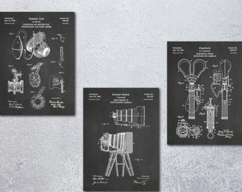 May include: Three framed vintage camera patent prints on a chalkboard background. The prints are in black and white, showcasing detailed diagrams of camera components and designs. The text "Camera Iris", "Kinneer Camera", and "Flashbulb" are visible.