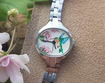 Petite montre-bracelet pour femme ovale vintage de couleur argentée sur bracelet en métal Ornement de colibri peint à la main. Montre à cadran blanc.