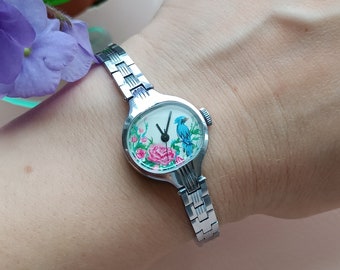Petite montre-bracelet mécanique vintage élégante pour femme avec cadran peint à la main, boîtier argenté sur un bracelet en métal fin.