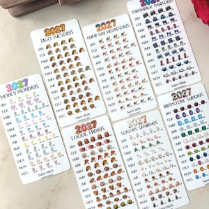 May include: A collection of seven white rectangular 2027 savings tracker stickers featuring monthly themes like Money Mondays, Taco Tuesdays, Hump Day Wednesdays, Throwback Thursdays, Foodie Fridays, Seasons Saturdays, and Birthstone Sundays.
