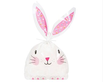 May include: White plastic treat bag with bunny ears. The ears are pink with white polka dots. The bag has a white bunny face with pink cheeks, a pink nose, and black whiskers.