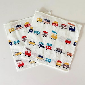 Könnte beinhalten: Zwei weiße Papierservietten mit einem sich wiederholenden Muster aus bunten Zugwaggons. Die Waggons sind in verschiedenen Farben gehalten, darunter Rot, Blau, Gelb und Braun, und sind durch eine schwarze Linie verbunden.