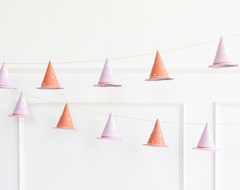 May include: A string of witch hats in pink and orange with white stars and moons hanging against a white wall.