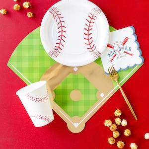 May include: A baseball-themed party table setting with a white paper plate featuring a red baseball design, a green and white checkered tablecloth with a gold baseball diamond, a white paper cup with a red baseball design, a gold fork, and a blue and white paper napkin with the text "All-Star Champion" and a baseball bat graphic.