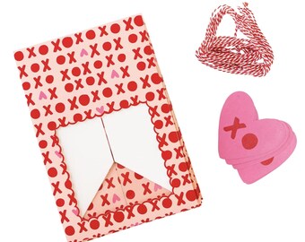 May include: A set of Valentine's Day gift tags featuring pink heart-shaped tags with red X's and a red and white twine. The tags are printed with a pink and red pattern of hearts and X's.