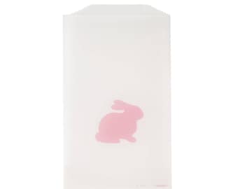 May include: A white paper bag with a pink bunny silhouette on the front. The bag is rectangular with a folded top edge. The bunny is a solid pink color and is centered on the bag.