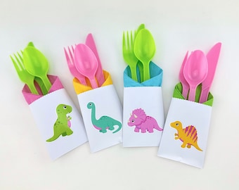 May include: Four white paper pouches each containing a plastic fork, spoon, and knife. The pouches feature colorful dinosaur illustrations and are lined with napkins in pink, yellow, blue, and green. The cutlery colors match the napkins.