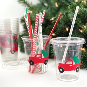 K&ouml;nnte beinhalten: Zwei durchsichtige Plastikbecher mit roten LKW- und Weihnachtsbaummotiven. Die Becher sind mit rot-wei&szlig; gestreiften Papierstrohhalmen, gr&uuml;n-wei&szlig; gestreiften Papierstrohhalmen und roten Papierstrohhalmen gef&uuml;llt.