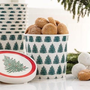 May include: A white paper container filled with sugared donuts, decorated with green Christmas trees. A stack of matching containers and a plate with a Christmas tree design are also visible, suggesting a holiday theme.