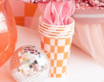 Puede incluir: Vasos de papel a cuadros naranja y blanco con tenedores de plástico rosa apilados en su interior. Una bola de discoteca plateada está en primer plano.