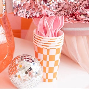 May include: Orange and white checkered paper cups with pink plastic forks stacked inside. A silver disco ball is in the foreground.
