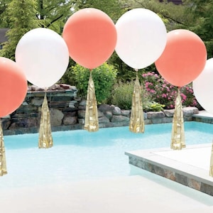 Peut inclure: Un ensemble de ballons ronds de grande taille, de couleur blanche et corail, disposés en arche au-dessus d'une piscine. Chaque ballon est orné d'une pampille dorée.
