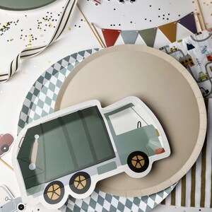 May include: A green and white paper plate with a cartoon illustration of a green garbage truck. The plate is on top of a beige paper plate with a diamond pattern.