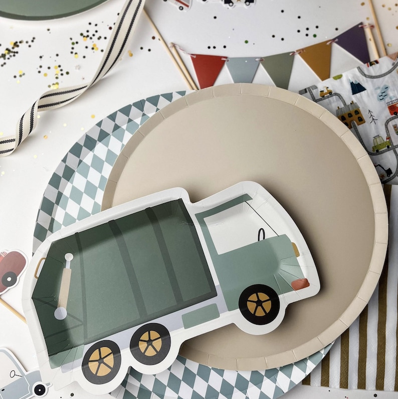 May include: A green and white paper plate with a cartoon illustration of a green garbage truck. The plate is on top of a beige paper plate with a diamond pattern.