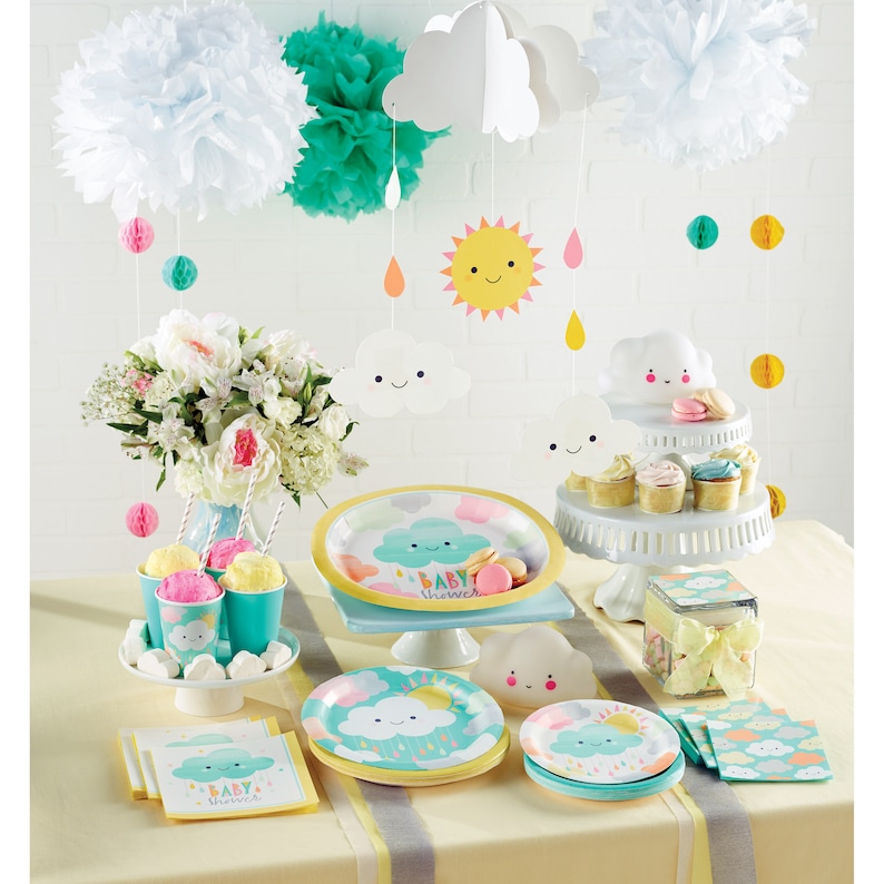 K&ouml;nnte beinhalten: Eine Babyparty-Tischdekoration in blau und gelber Farbgebung. Der Tisch ist mit Papptellern, Servietten und Bechern mit einem Wolken- und Regentropfen-Design dekoriert. Es gibt einen Kuchenst&auml;nder mit Cupcakes und einen durchsichtigen Beh&auml;lter mit einer gelben Schleife. Der Tisch ist au&szlig;erdem mit wei&szlig;en und gr&uuml;nen Seidenpapier-Pompons sowie h&auml;ngenden Papierwolken und einer Sonne dekoriert.