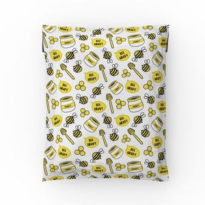 Könnte beinhalten: Weiße Poly-Versandtaschen mit einem sich wiederholenden Muster aus gelben Bienen, Honigwaben und Honiggläsern. Der Text "Bee Happy" wird im gesamten Muster wiederholt.