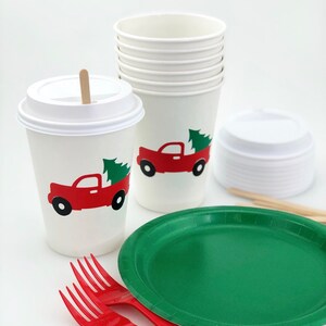 May include: White paper cups and lids, a green paper plate, and red plastic forks. The cups feature a red truck carrying a green Christmas tree. A wooden stir stick is in one cup.