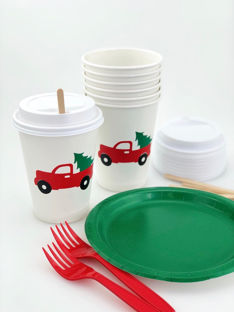 May include: White paper cups and lids, a green paper plate, and red plastic forks. The cups feature a red truck carrying a green Christmas tree. A wooden stir stick is in one cup.