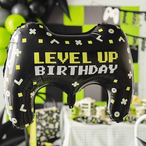 Op de afbeelding: Zwarte en gele gamer-thema ballon in de vorm van een videogamecontroller met de tekst "Level Up Birthday".