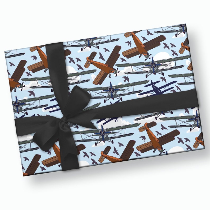 May include: A blue and white gift wrapping paper with a repeating pattern of brown and blue airplanes flying in a sky with white clouds. The paper is tied with a black ribbon.