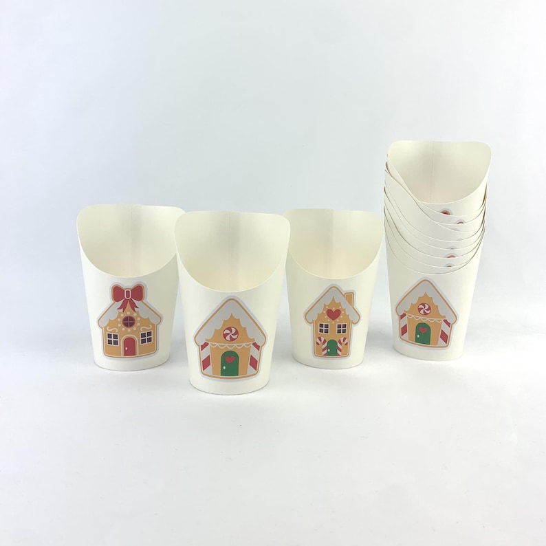 Puede incluir: Conjunto de vasos de papel blancos con dise&ntilde;os de casas de jengibre. Los vasos son perfectos para servir aperitivos o golosinas en una fiesta navide&ntilde;a.
