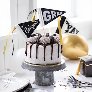 May include: A white cake with chocolate frosting and Oreo cookies on top. The cake is decorated with black and white graduation flags that say "Congrats", "Grad", and "Yay".