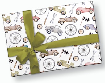 May include: A white gift box with a green ribbon and bow. The box is wrapped in paper with a repeating pattern of vintage cars, spanners, screwdrivers, and tyres.