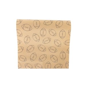 May include: Brown wrapping paper with a repeating pattern of black footballs. The footballs are outlined with black lines and have detailed stitching. The paper is folded, showing the pattern on the front.