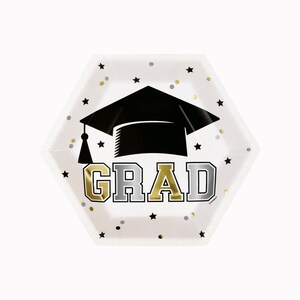 May include: A white, hexagonal paper plate with a black graduation cap and the word "GRAD" in gold and silver lettering. The plate is decorated with black stars and gold and silver confetti.
