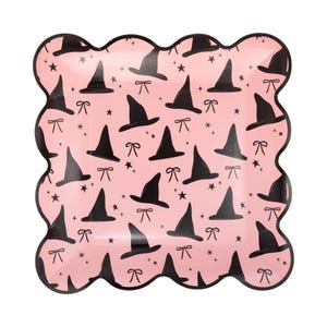 May include: A pink, scalloped-edge paper plate with a repeating pattern of black witch hats, bows, and stars. The plate is designed for Halloween or themed parties.