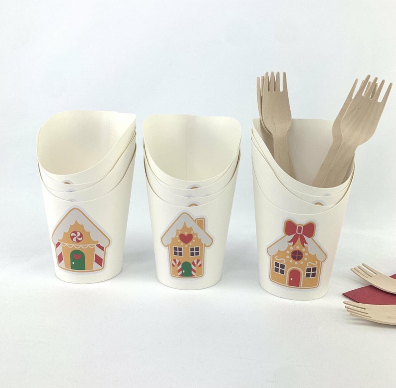 Puede incluir: Conjunto de tres vasos de papel blanco con dise&ntilde;os de casas de jengibre. Cada vaso tiene un dise&ntilde;o diferente con detalles rojos, verdes y blancos. Los vasos est&aacute;n apilados uno encima del otro.
