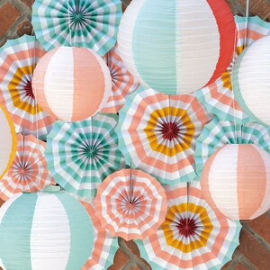 May include: A collection of paper fans and paper lanterns in various colors and patterns, including pink, blue, yellow, and white. The fans are folded and have a striped design, while the lanterns are round and have a striped or solid color design.