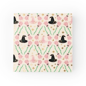 May include: A square, cream-colored paper product with a repeating pattern of witch hats, pink brooms, gold stars, and crescent moons. The witch hats are black and pink. The brooms have green handles.