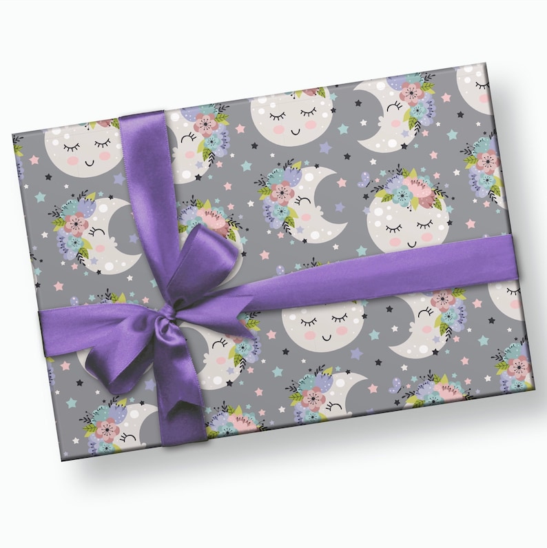 May include: A gray gift wrap with a repeating pattern of sleeping crescent moons with floral wreaths and stars. The gift is wrapped with a purple ribbon and bow.