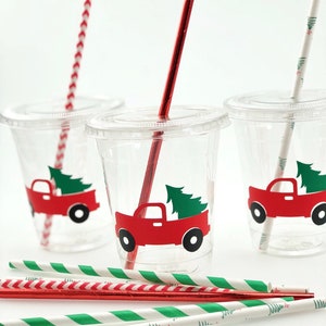 K&ouml;nnte beinhalten: Drei durchsichtige Plastikbecher mit rot-wei&szlig; gestreiften Strohhalmen und gr&uuml;n-wei&szlig; gestreiften Strohhalmen. Jeder Becher hat einen roten Lastwagen mit einem gr&uuml;nen Weihnachtsbaum hinten drauf. Der Lastwagen hat einen wei&szlig;en Umriss.