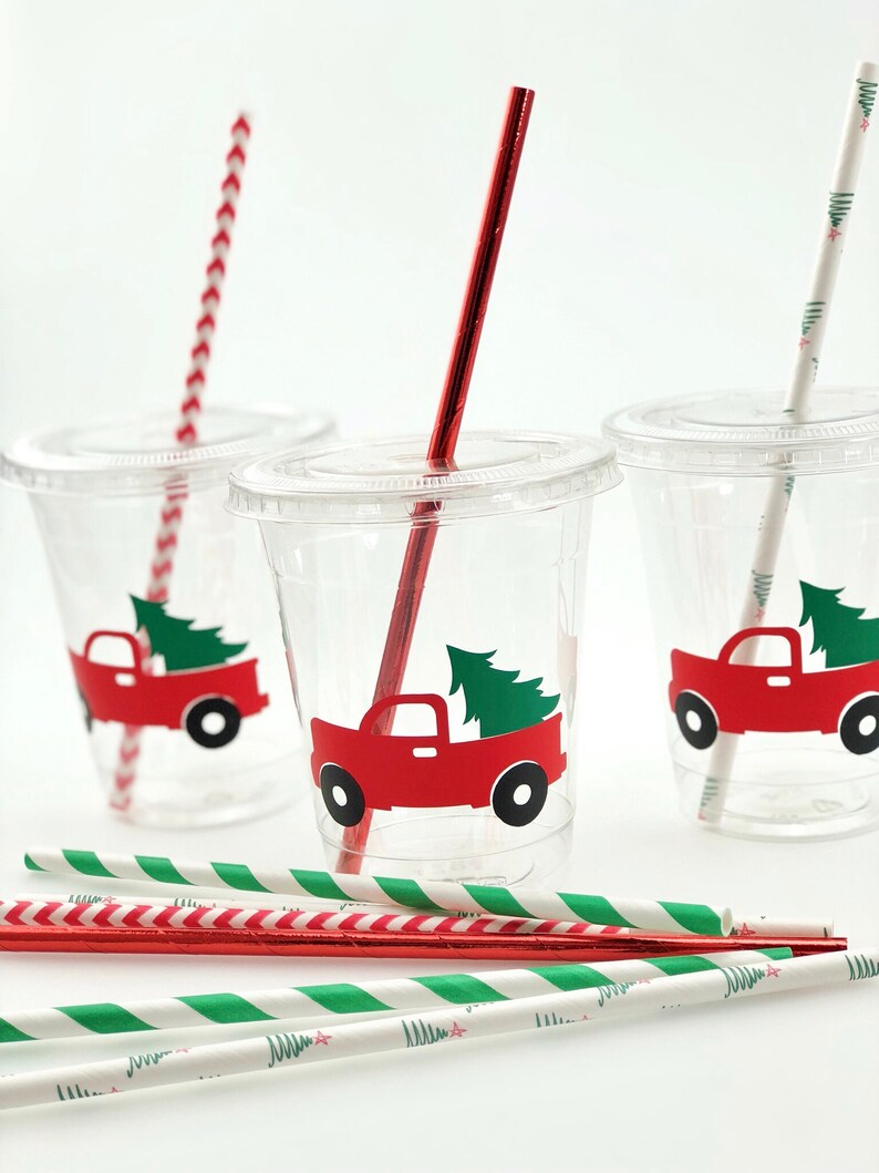 K&ouml;nnte beinhalten: Drei durchsichtige Plastikbecher mit rot-wei&szlig; gestreiften Strohhalmen und gr&uuml;n-wei&szlig; gestreiften Strohhalmen. Jeder Becher hat einen roten Lastwagen mit einem gr&uuml;nen Weihnachtsbaum hinten drauf. Der Lastwagen hat einen wei&szlig;en Umriss.