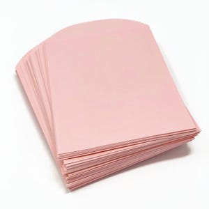 Puede incluir: Una pila de hojas de papel rosa claro, cada una con un borde superior curvo. El papel está apilado, revelando las hojas individuales. El fondo es blanco, ofreciendo un contraste limpio con el papel rosa.