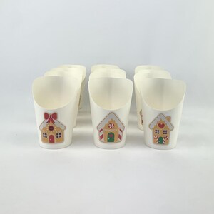 Puede incluir: Ocho vasos de papel blancos con un dise&ntilde;o de casa de jengibre. Las casas est&aacute;n decoradas con detalles rojos y verdes.