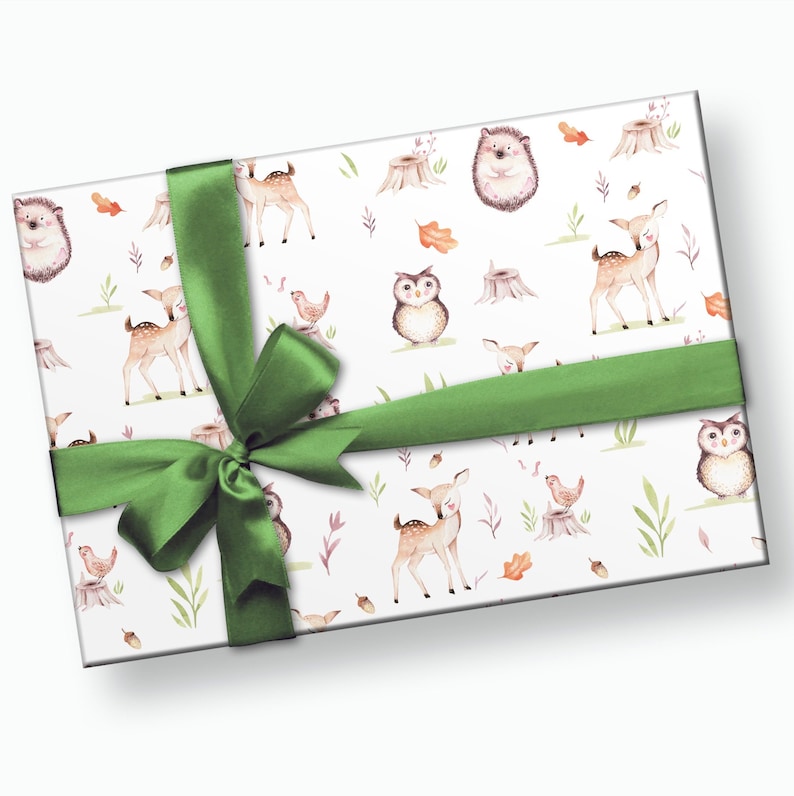 Puede incluir: Un papel de regalo blanco con un lazo de cinta verde. El papel de regalo presenta un patr&oacute;n repetitivo de animales del bosque, incluyendo ciervos, b&uacute;hos y erizos. Los animales est&aacute;n ilustrados en un estilo de acuarela.