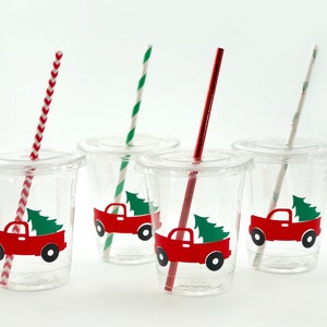 K&ouml;nnte beinhalten: Vier durchsichtige Plastikbecher mit roten und gr&uuml;nen Weihnachts-LKW-Designs und rot-wei&szlig; gestreiften Strohhalmen.