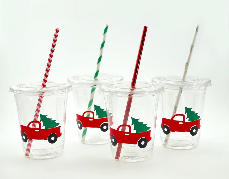 K&ouml;nnte beinhalten: Vier durchsichtige Plastikbecher mit roten und gr&uuml;nen Weihnachts-LKW-Designs und rot-wei&szlig; gestreiften Strohhalmen.