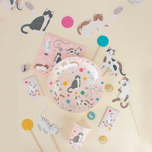 May include: A pink and white cat-themed party supply set with plates, cups, napkins, and decorations. The set features a variety of cats in different poses, including playing with yarn and a mouse.