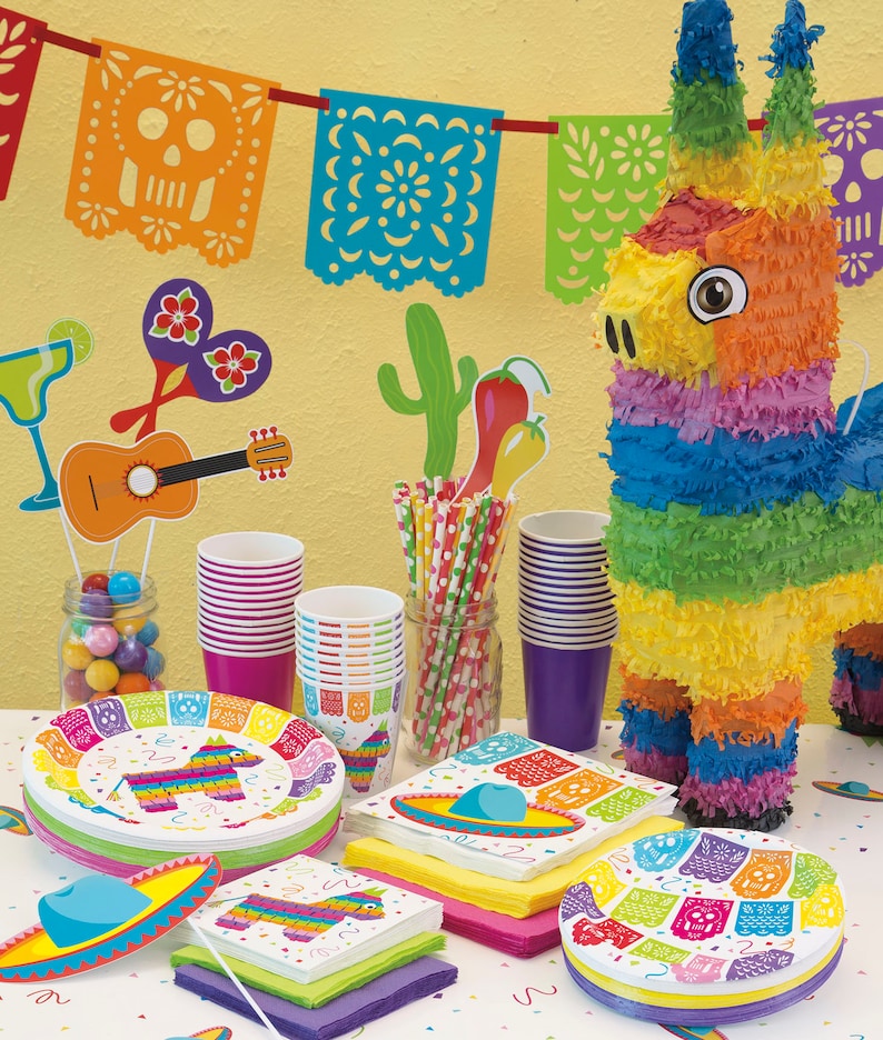 May include: A colorful fiesta party supplies set with a pinata, paper plates, napkins, cups, and straws. The plates and napkins feature a pinata design with a skull and crossbones. The cups are red and purple. The straws are striped red and white.