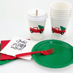 May include: A festive holiday party set featuring white paper cups with a red truck and Christmas tree design, green plates, red forks, and napkins with the text "Baby it's cold outside."