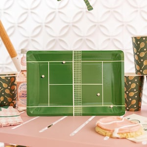 May include: Green paper party plates with a tennis court design. The plates feature a white net and two white tennis balls.