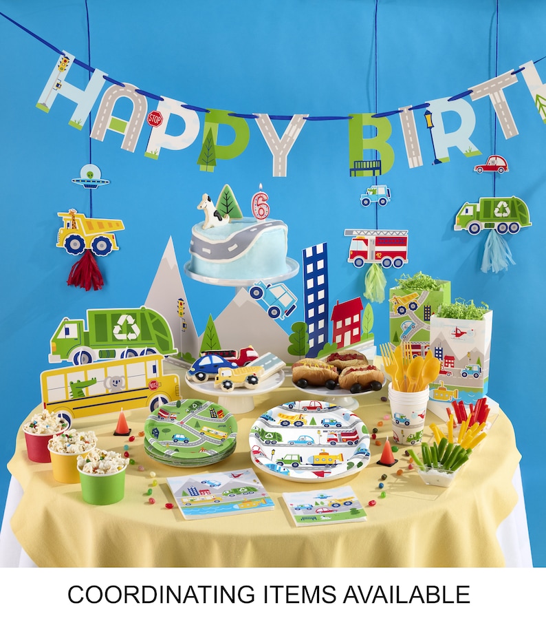 May include: A festive birthday party setup with a blue backdrop and a yellow tablecloth. The scene includes a cake, plates, cups, and decorations featuring a road and vehicle theme. A banner spells out "HAPPY BIRTH".