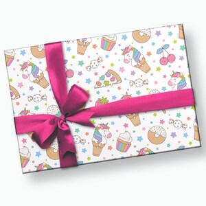 Puede incluir: Papel de regalo blanco con una cinta rosa y un patr&oacute;n repetido de unicornios, conos de helado, donuts, cupcakes, rebanadas de pizza, cerezas, caramelos y estrellas.