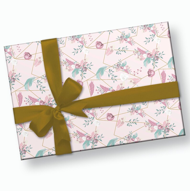 K&ouml;nnte beinhalten: Ein rechteckiger Geschenkkarton, der in rosa floral gemustertes Papier mit goldenen geometrischen Linien verpackt ist. Das Design umfasst rosa Rosen, wei&szlig;e Blumen und t&uuml;rkisfarbene Federn. Ein goldenes Satinband ist um die Schachtel gebunden.